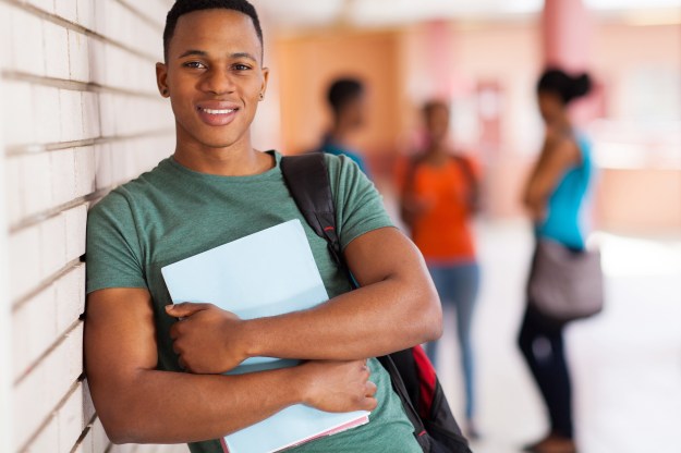 happy african american college student leaning against campus wa